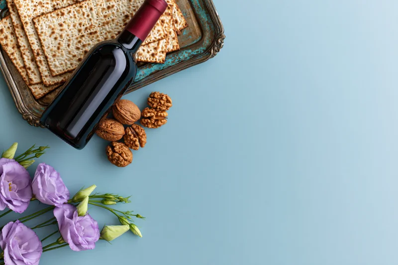 Matzah crackers and wine on a tarnished tray with walnuts and purple flowers on a blue surface