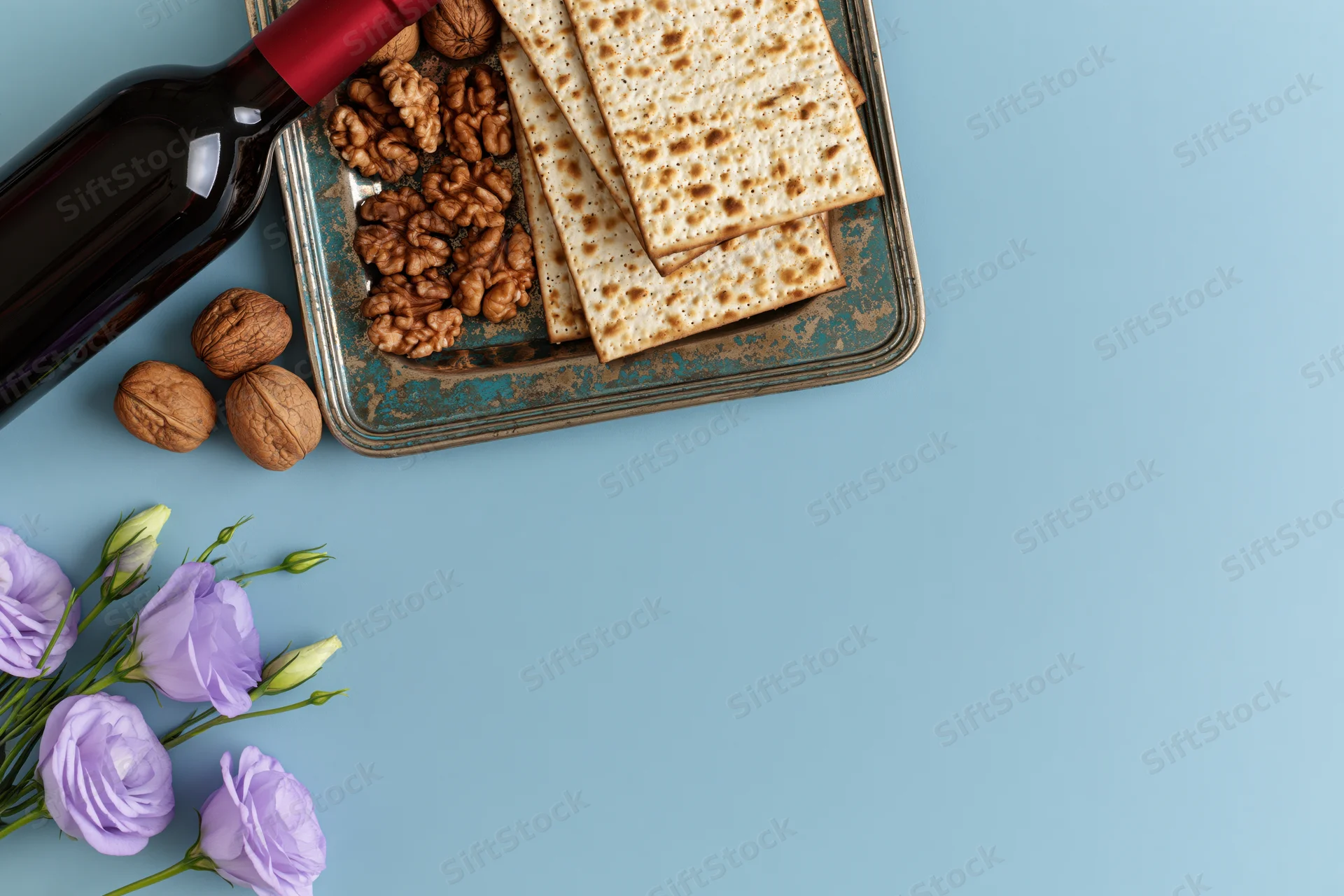 Matzah crackers and red wine on a tarnished tray with walnuts and purple flowers on a blue surface