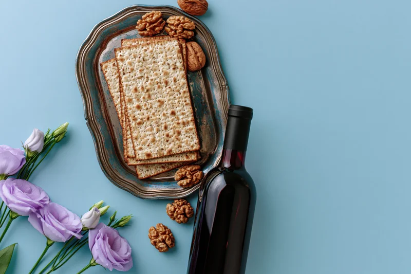 Matzah crackers and wine on a silver tray with flowers and walnuts for passover seder flat lay