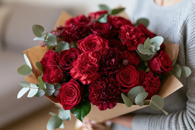 Woman holding a large bouquet of red roses and carnations wrapped in brown paper