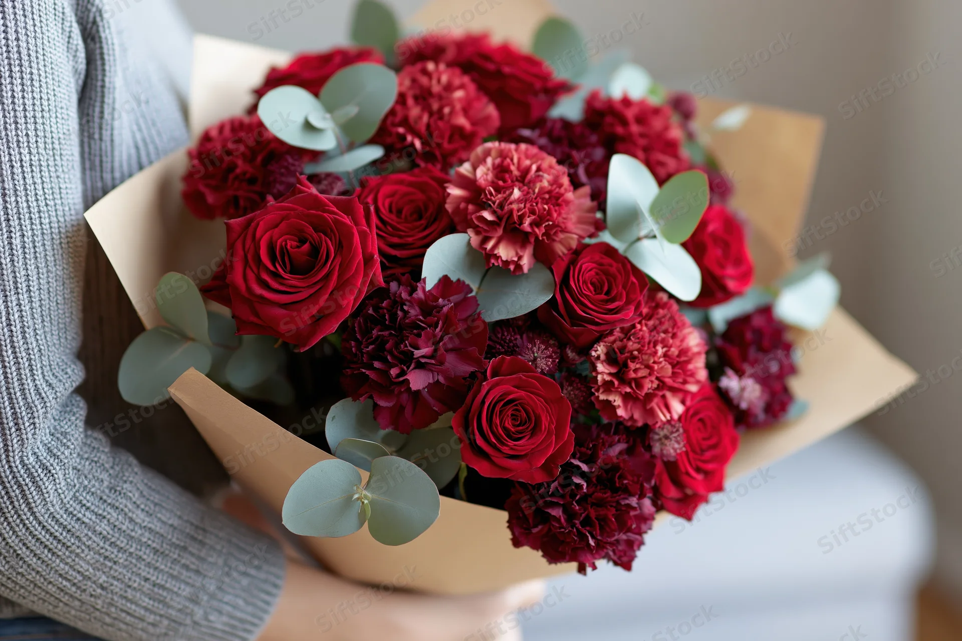 Woman holding a large mixed bouquet of deep red and crimson roses and carnations wrapped in kraft paper