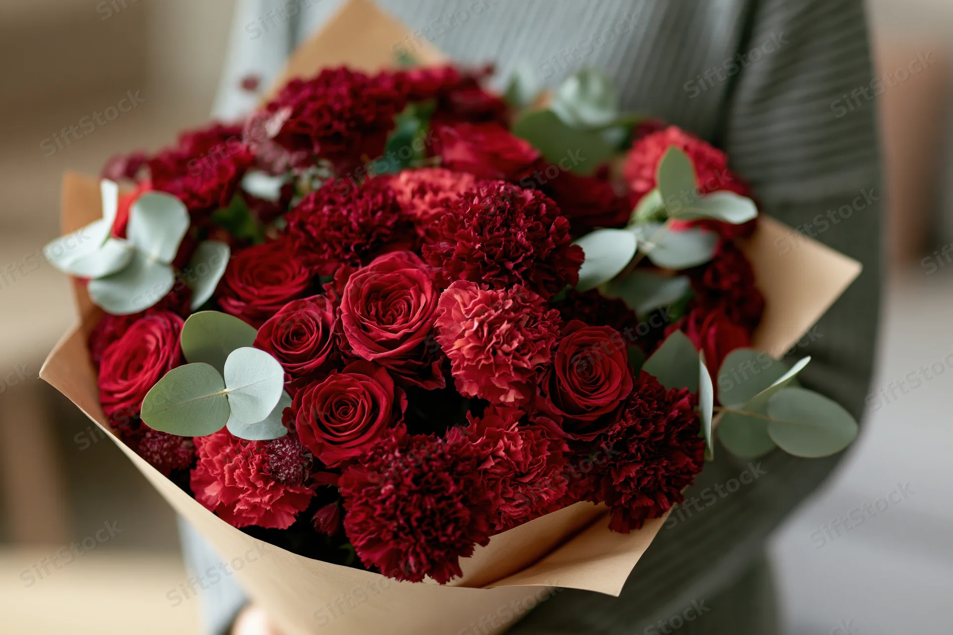 Woman holding a large bouquet of red roses and carnations wrapped in brown paper