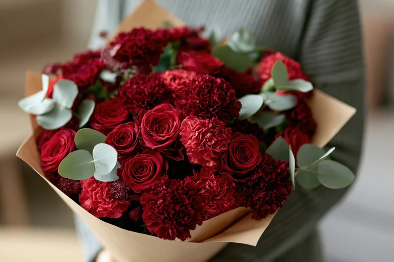 Woman holding a large bouquet of red roses and carnations wrapped in brown paper