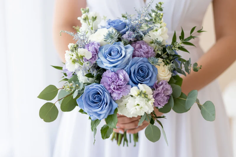 Bride holding a lush bridal bouquet of blue roses and lavender flowers with eucalyptus greenery