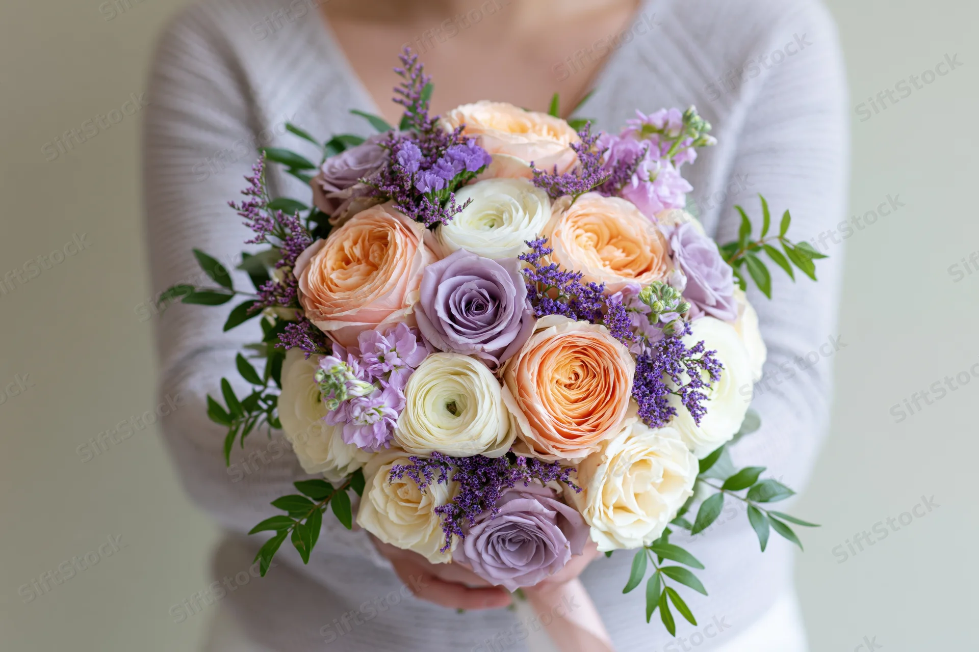 Woman holding a lush mixed bouquet of peach, lavender, and cream roses with greenery