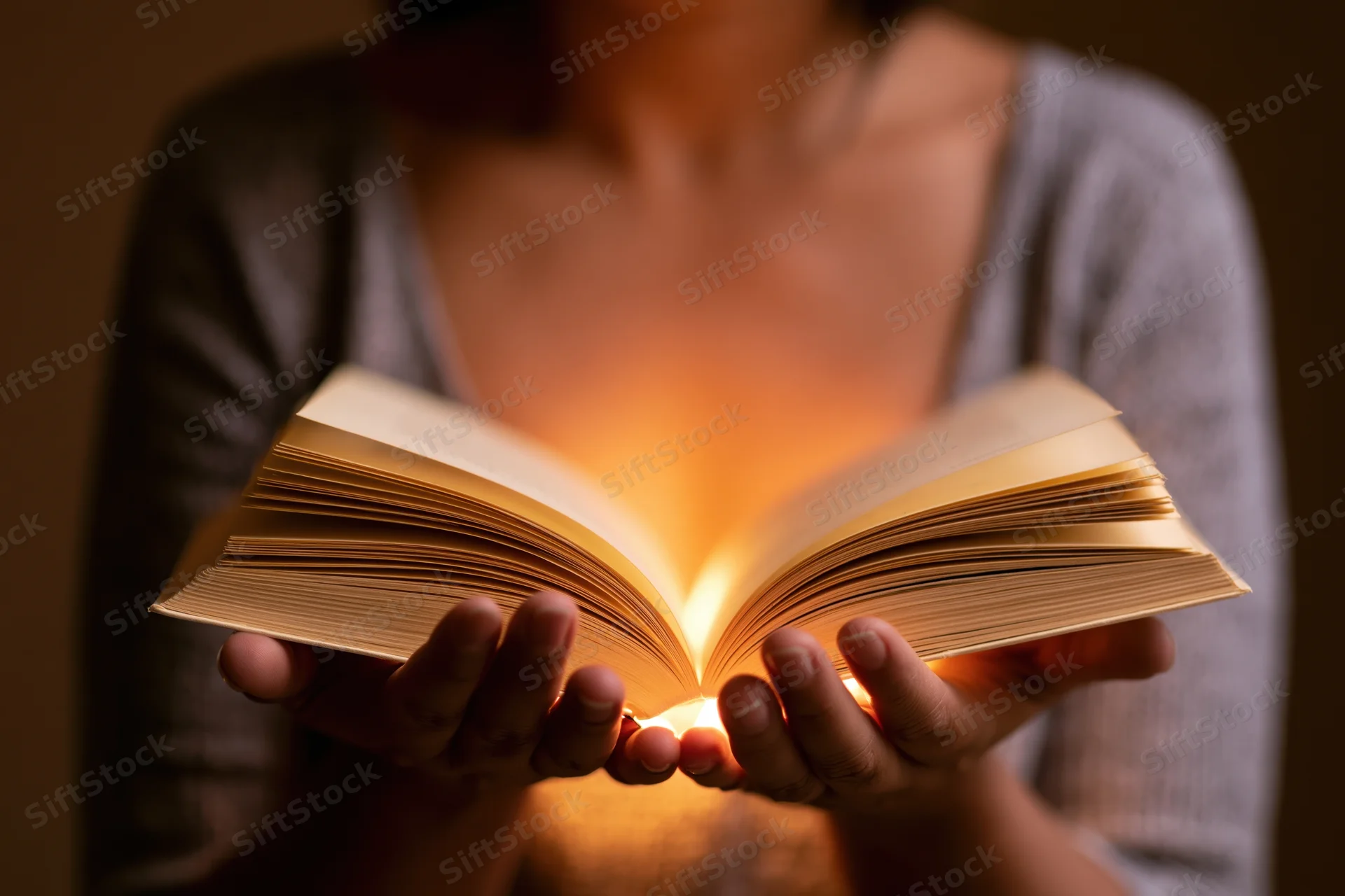 Woman holding open book with glowing pages in dim indoor setting