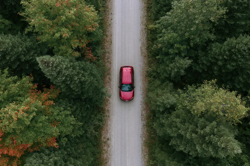 Red compact suv driving on narrow gravel road through forested area