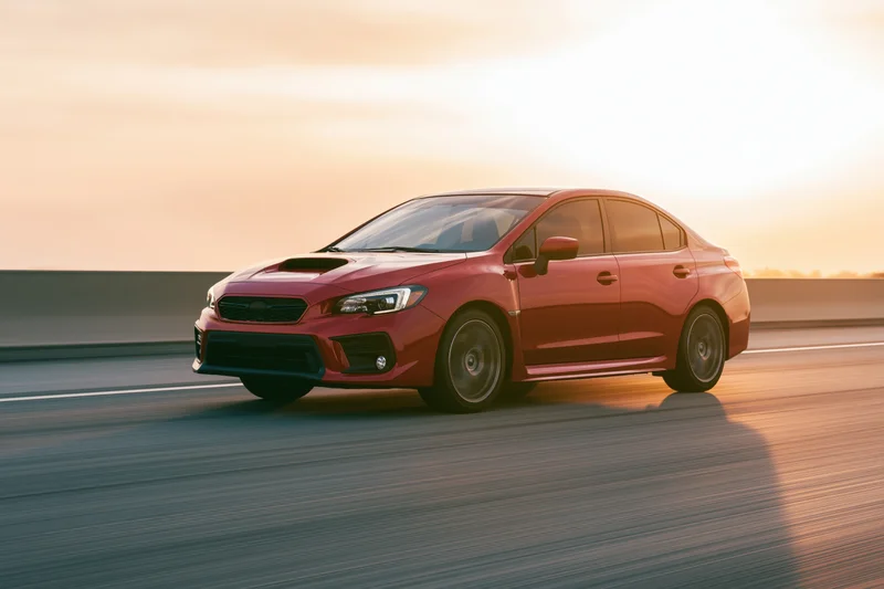 Red sport sedan driving fast on open highway at sunset