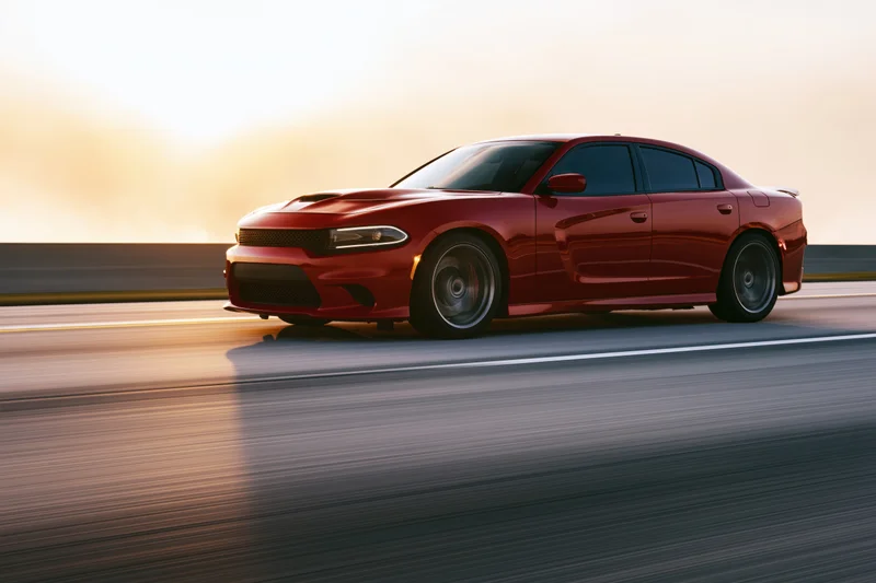 Red sport sedan driving fast on open highway at sunset