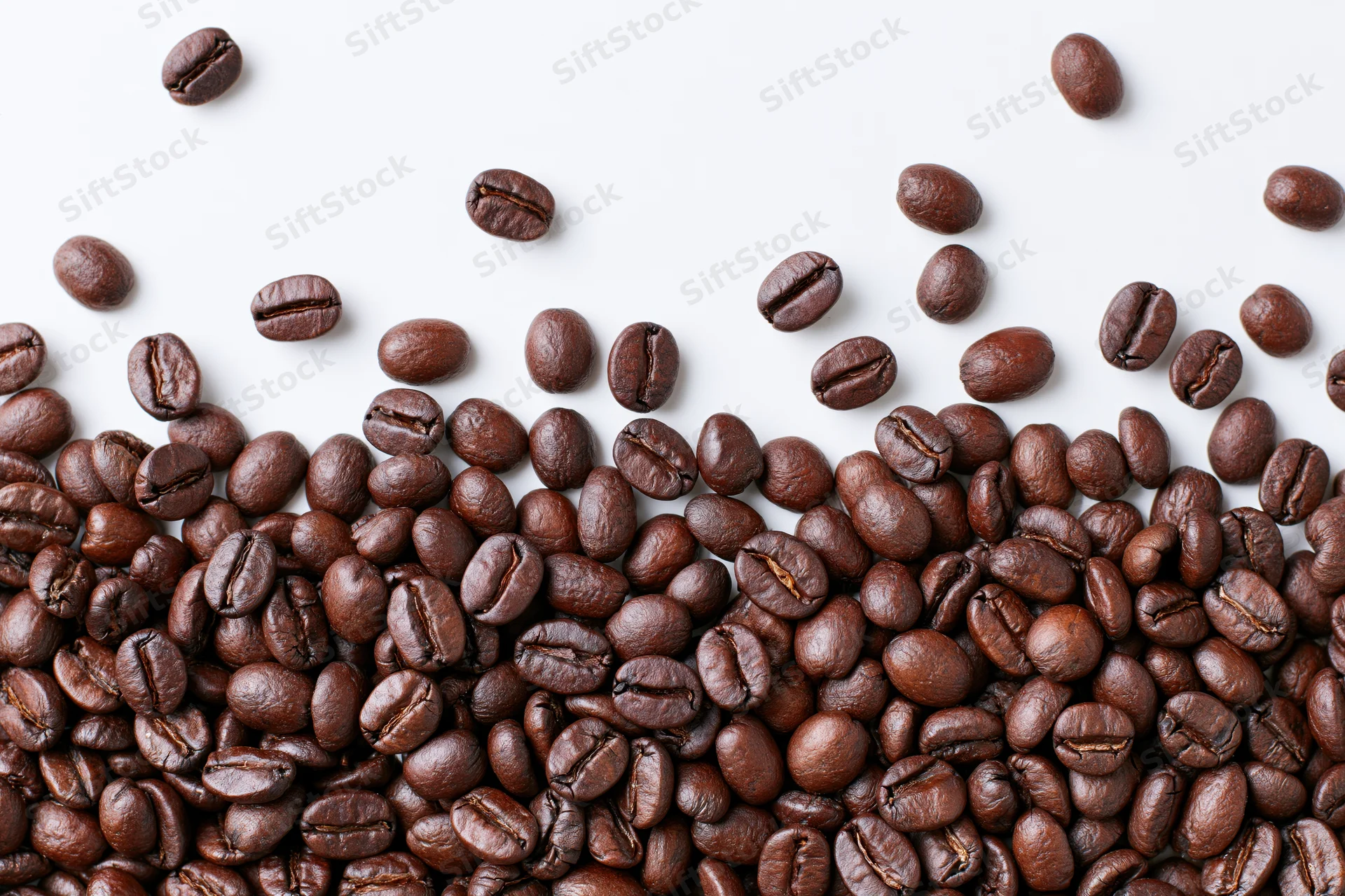 Roasted coffee beans scattered across a plain white surface in a flat lay composition