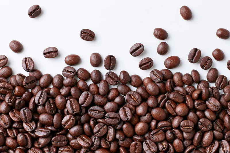 Roasted coffee beans scattered across a plain white surface in a flat lay composition