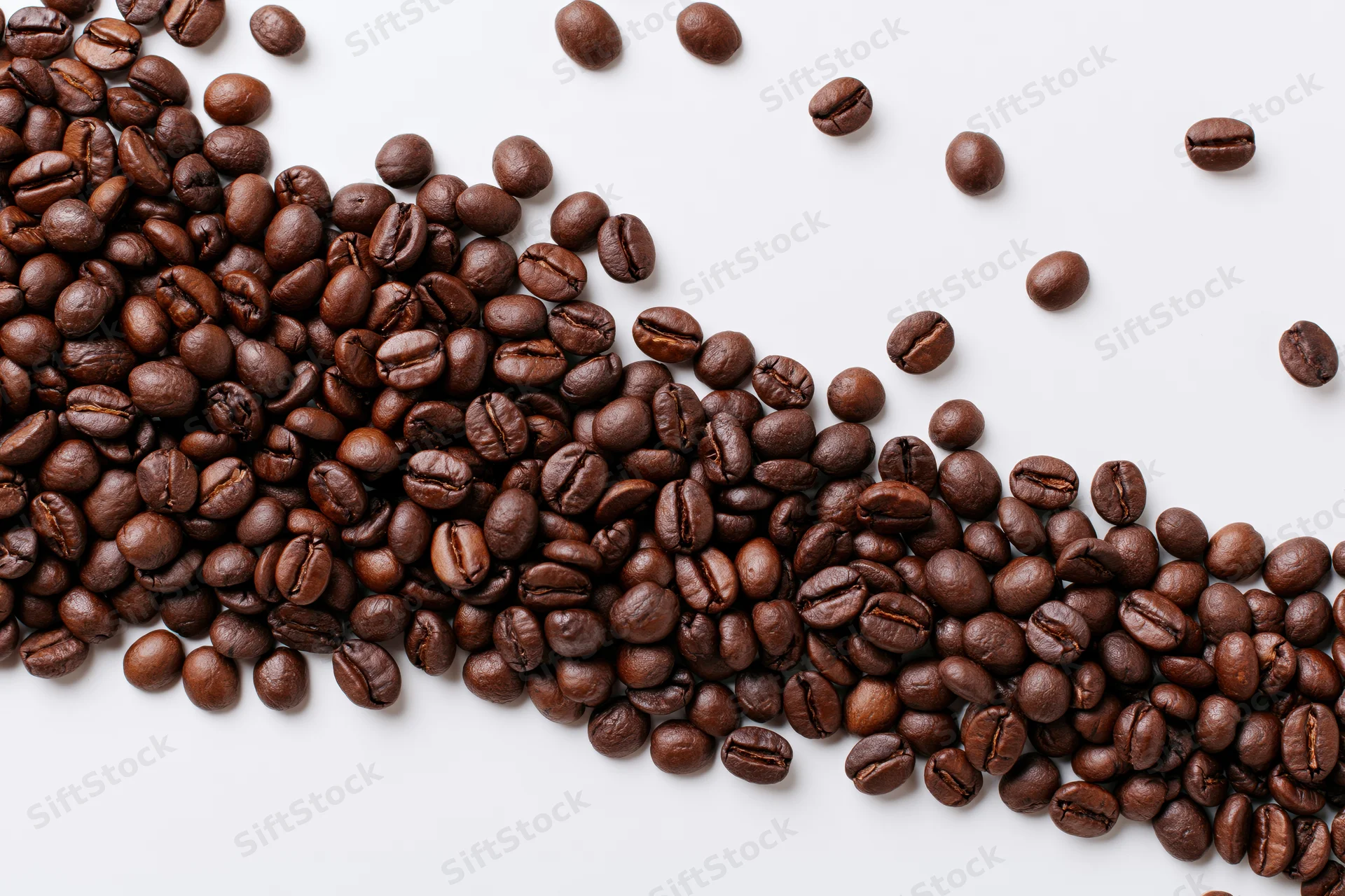 Roasted coffee beans scattered across a plain white surface