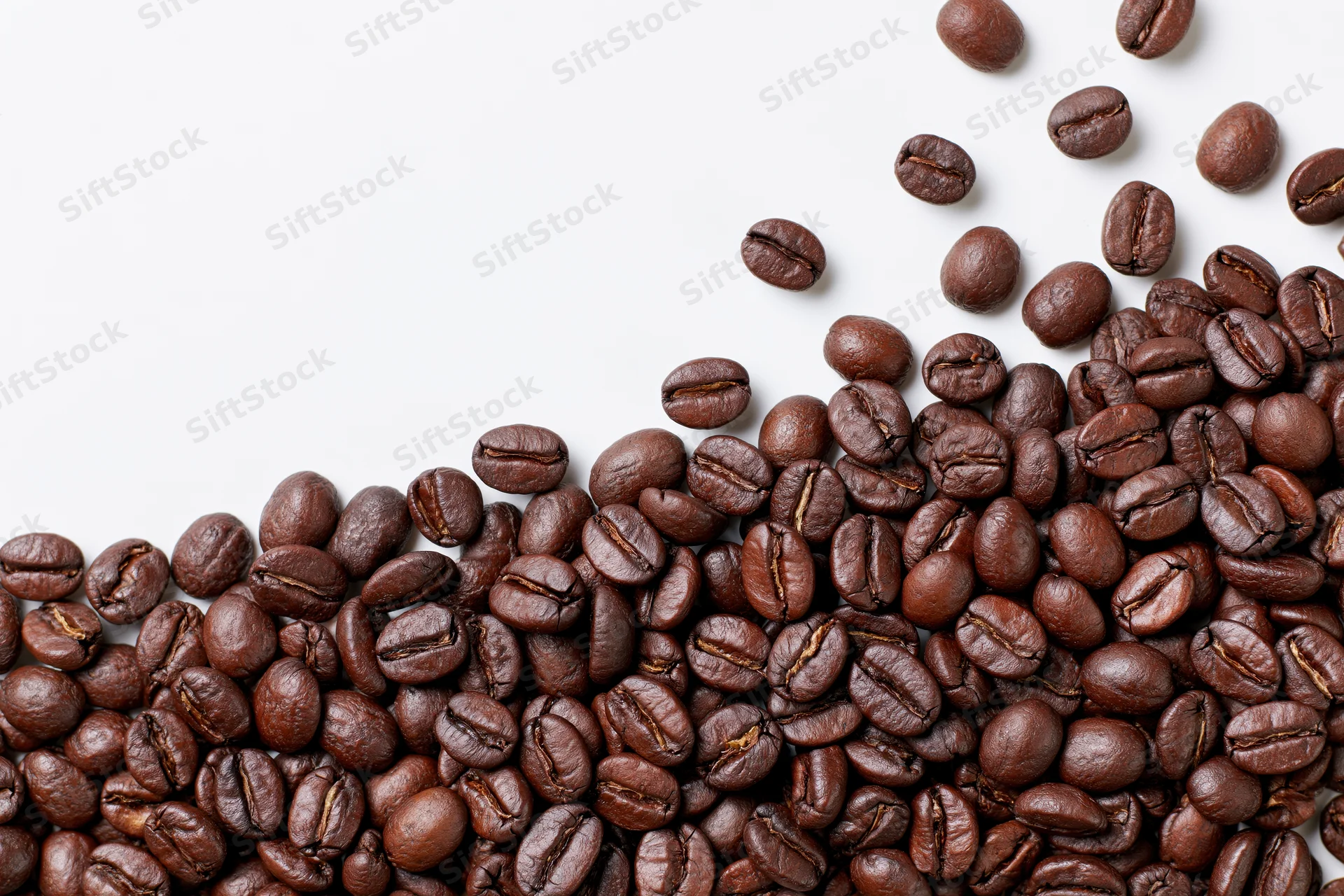 Roasted coffee beans scattered across a plain white surface in a flat lay composition