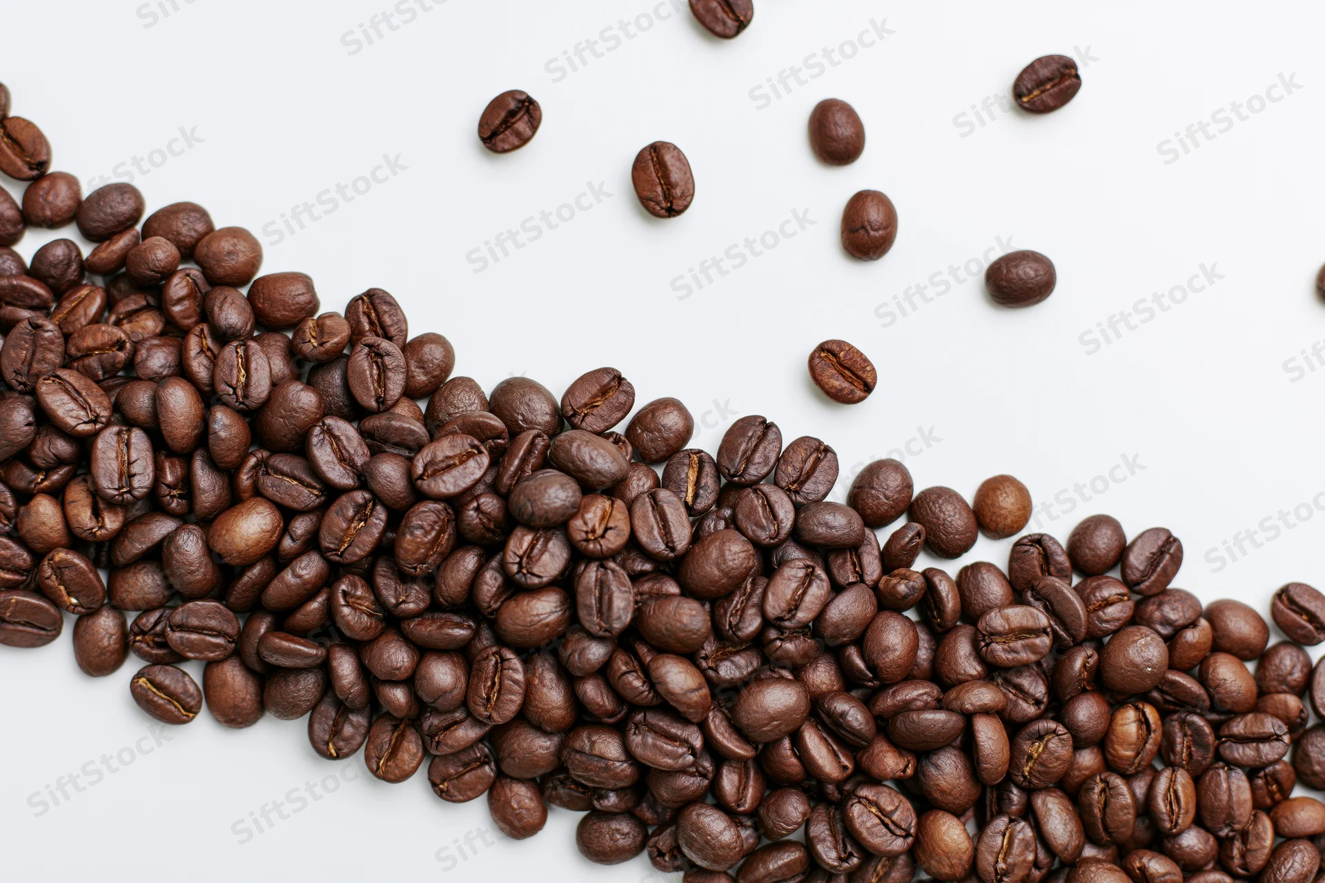 Roasted coffee beans scattered across a plain white surface