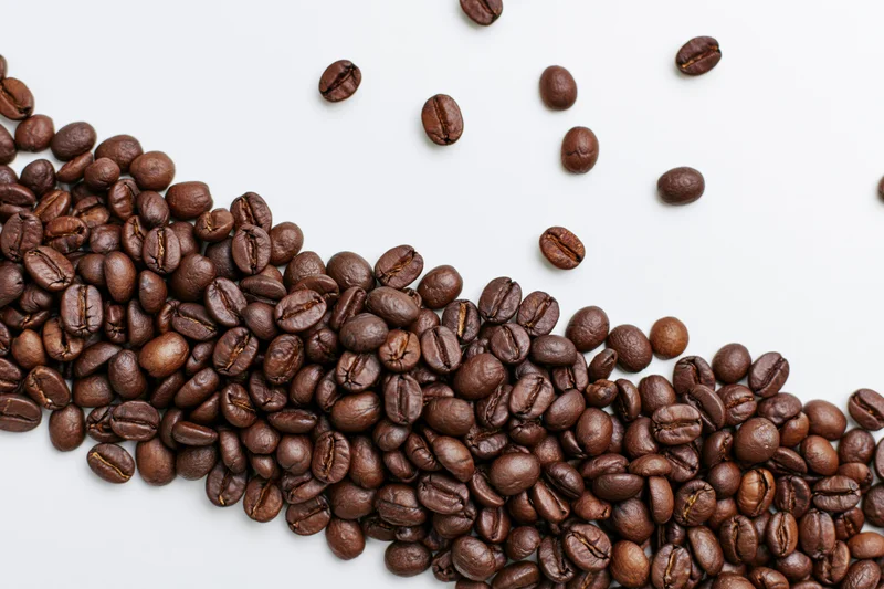 Roasted coffee beans scattered across a plain white surface