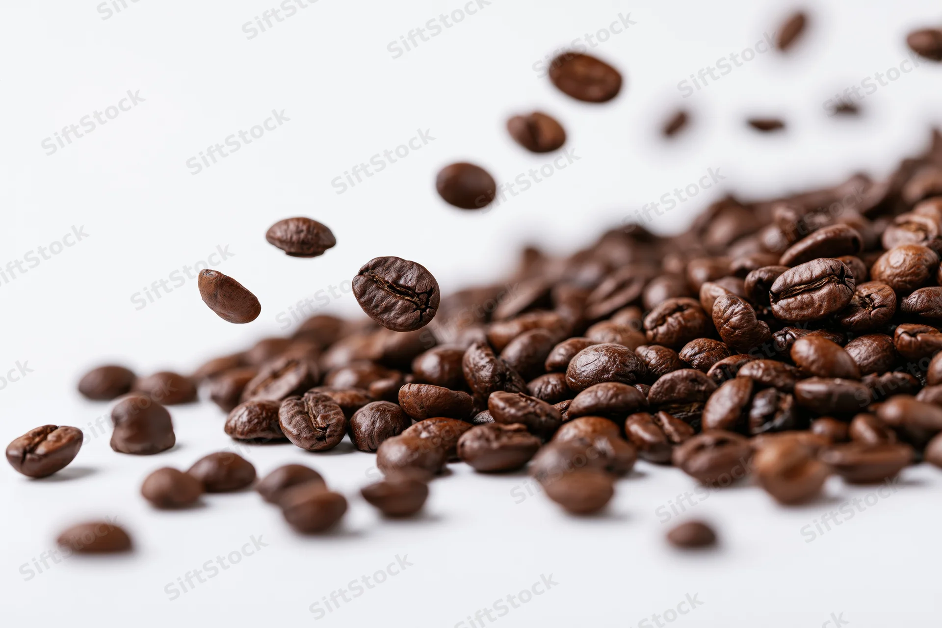 Roasted coffee beans falling midair and scattered in a diagonal pile on white background