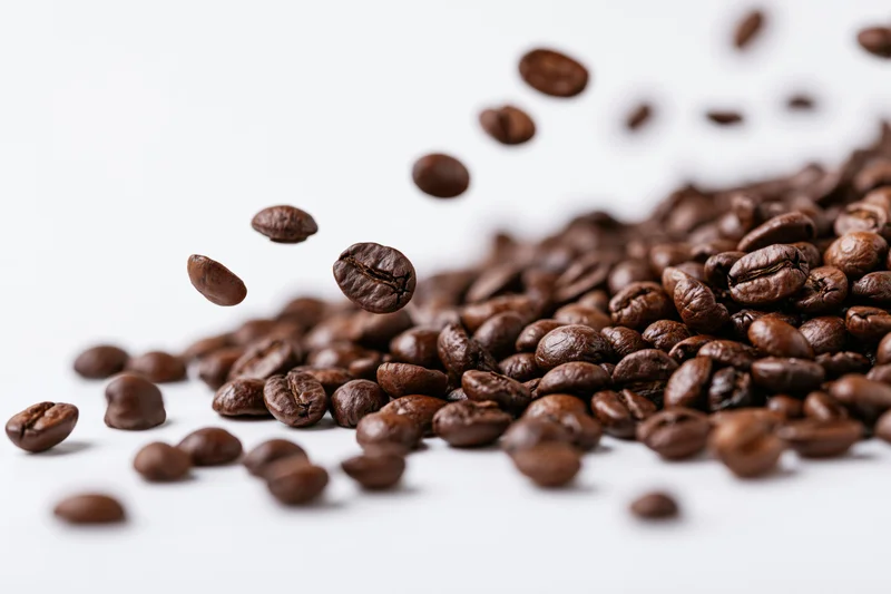 Roasted coffee beans falling midair and scattered in a diagonal pile on white background