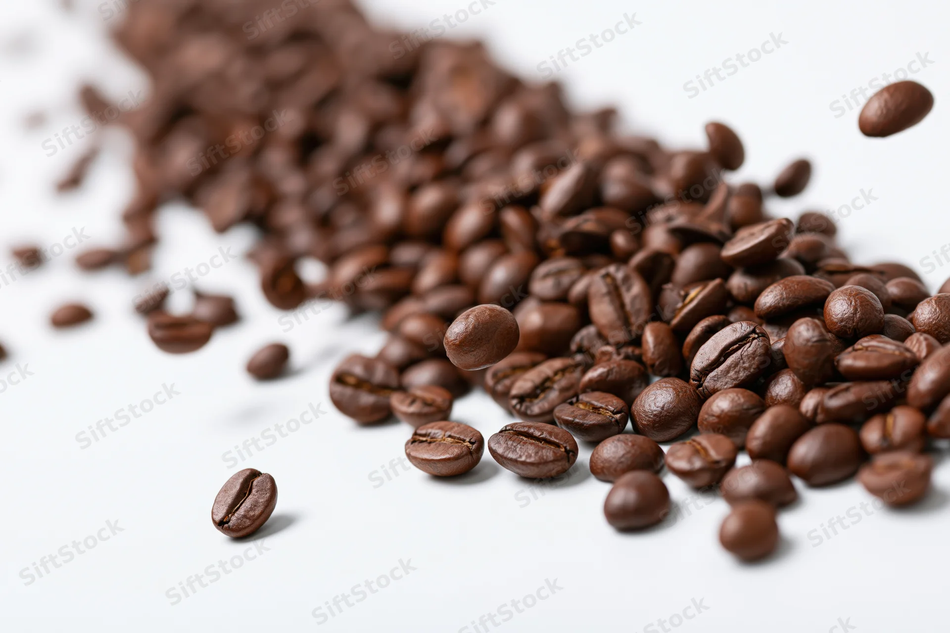 Roasted coffee beans falling and scattered diagonally on a white surface