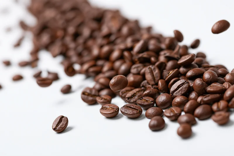 Roasted coffee beans falling and scattered diagonally on a white surface