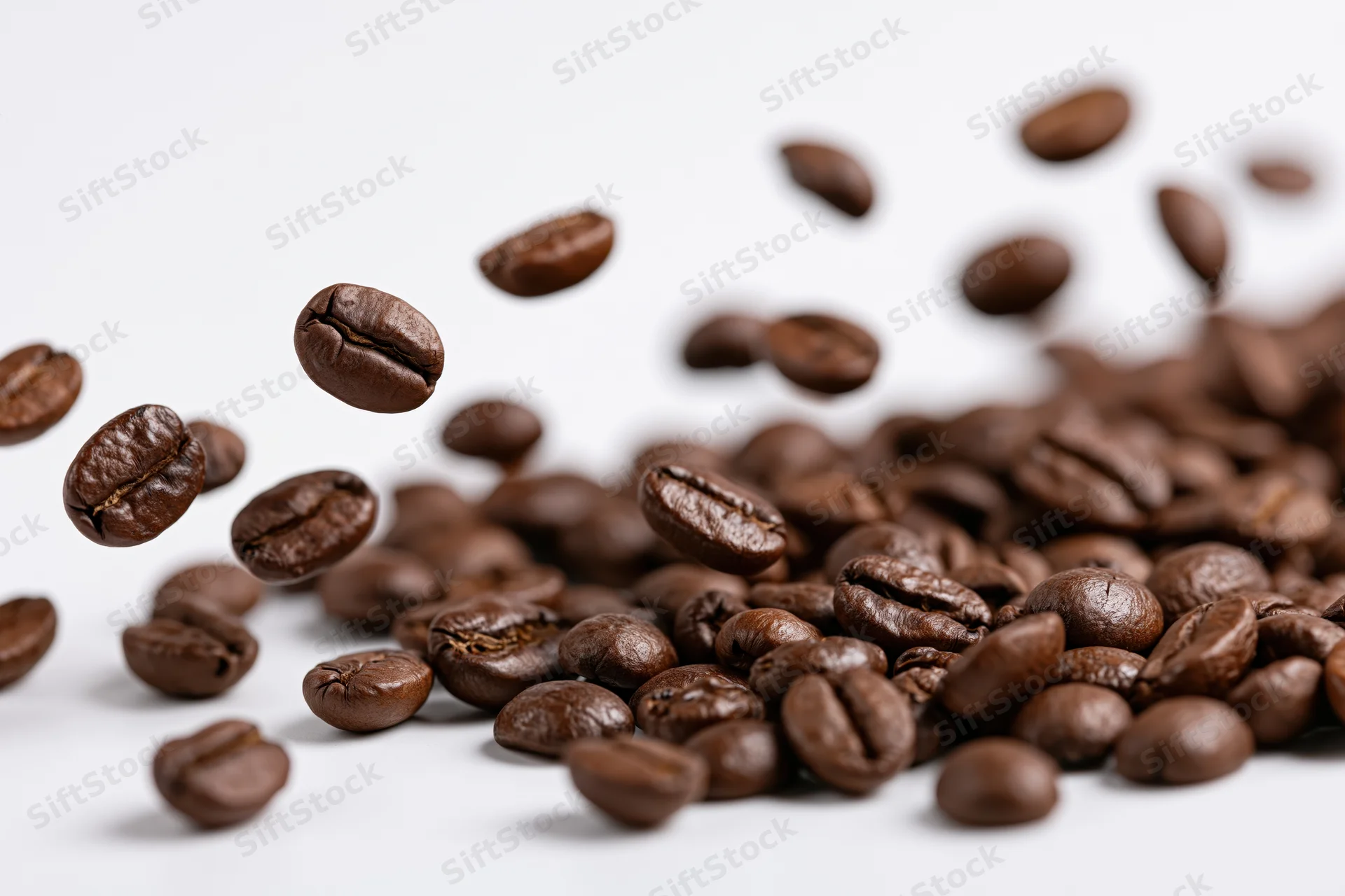 Roasted coffee beans falling midair and scattered on white surface