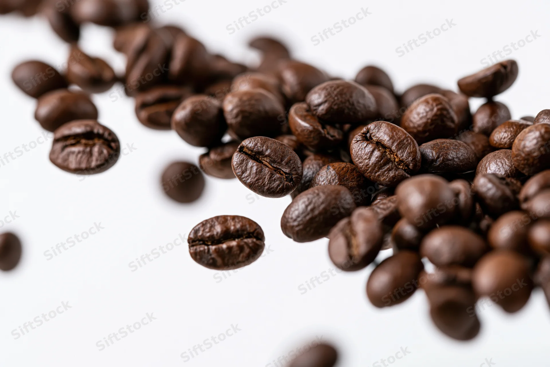 Roasted coffee beans falling midair in diagonal pattern against white background