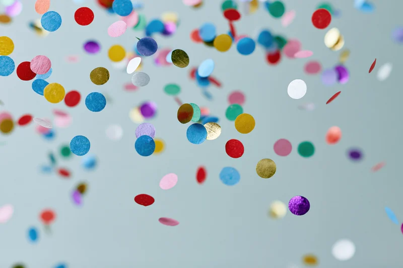 Round confetti pieces floating midair against a light blue background