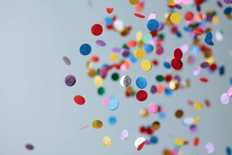 Round confetti pieces floating midair against a light gray background with copyspace on the left