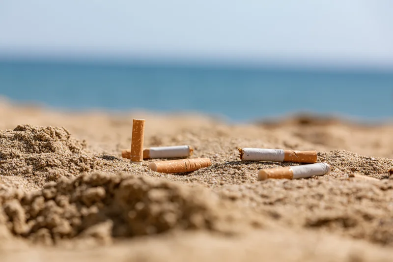 Cigarette butts scattered on sandy beach near ocean