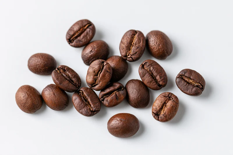 Dark roasted coffee beans scattered in loose clusters on white background