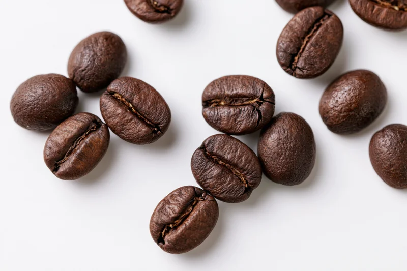 Dark roasted coffee beans scattered in loose clusters on white surface