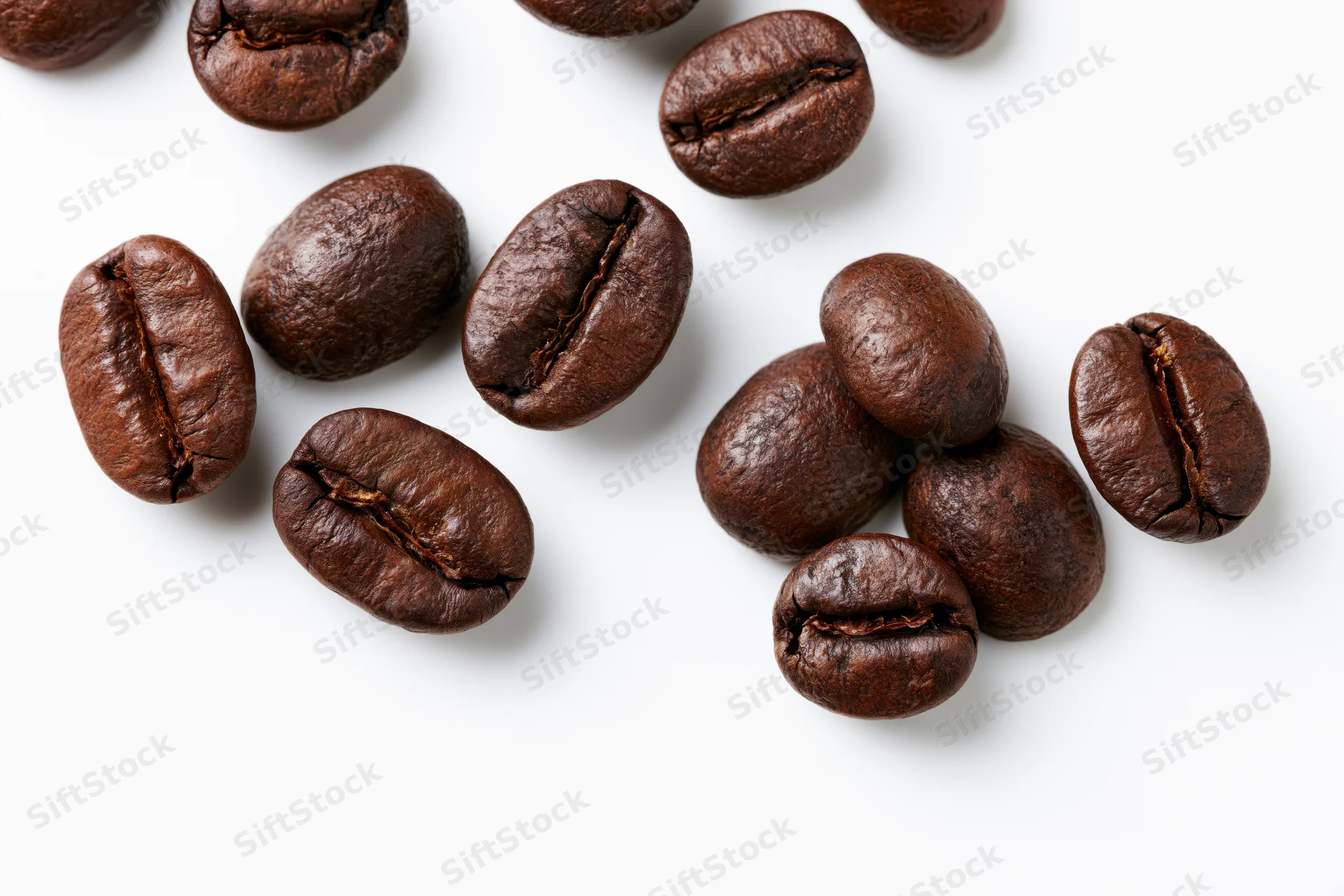 Dark roasted coffee beans scattered in loose clusters on white background