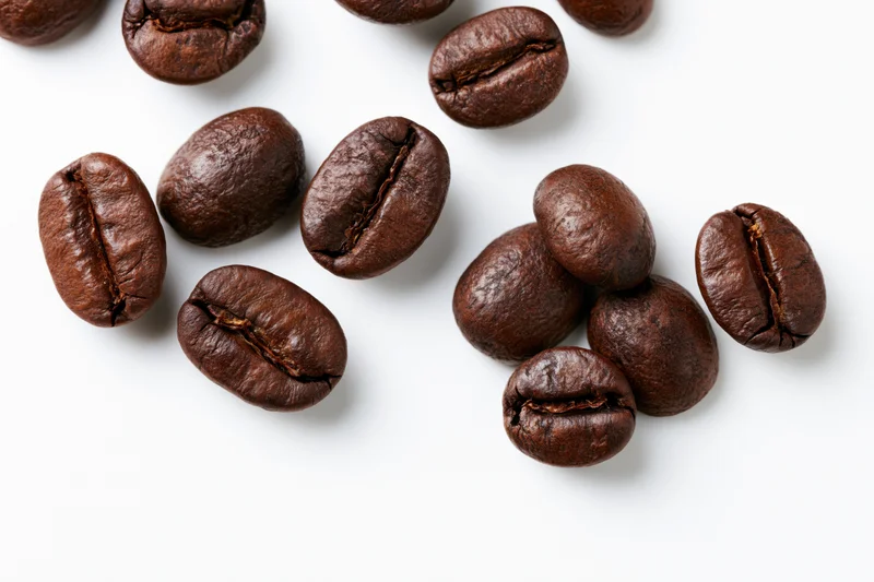 Dark roasted coffee beans scattered in loose clusters on white background
