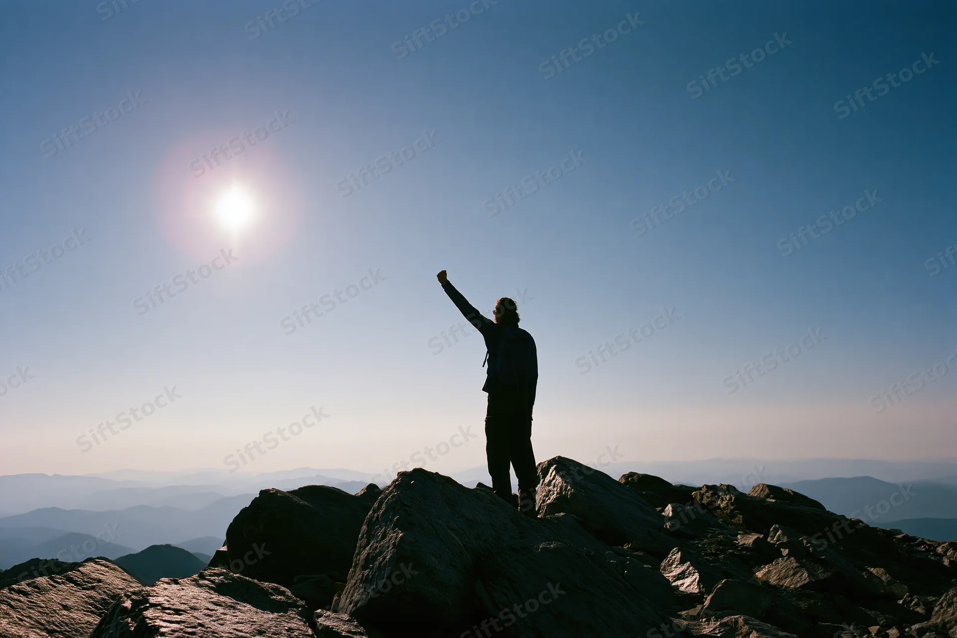 Hiker standing on rocky mountain summit with arm raised toward sun