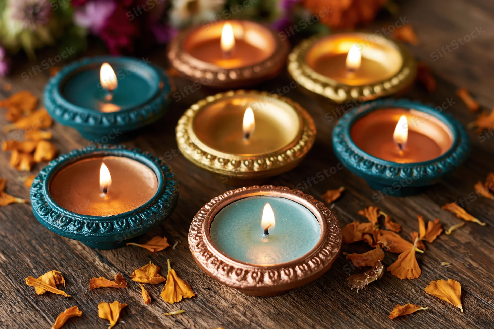 Six lit diya oil lamps arranged on wooden surface with scattered flower petals and warm glow