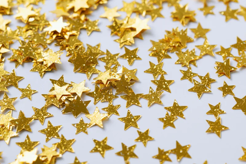 Gold foil star confetti scattered randomly on white surface