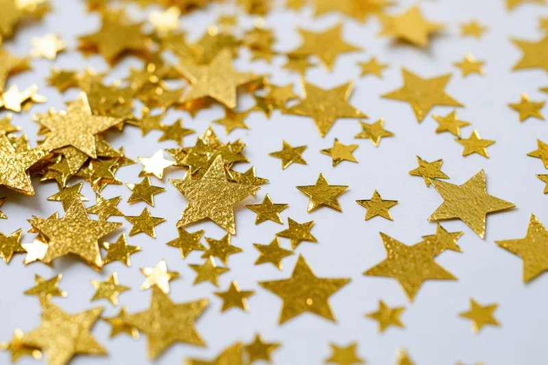 Gold foil star confetti scattered randomly on white surface