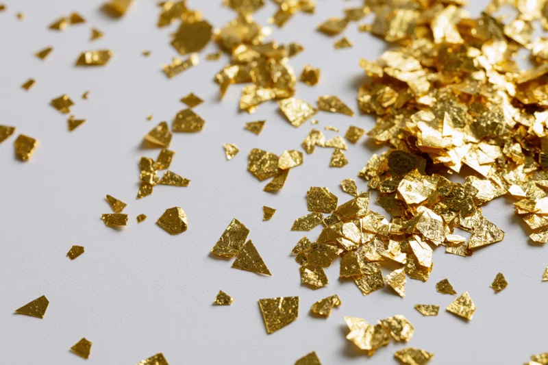 Scattered gold foil confetti pieces on a white surface with copyspace