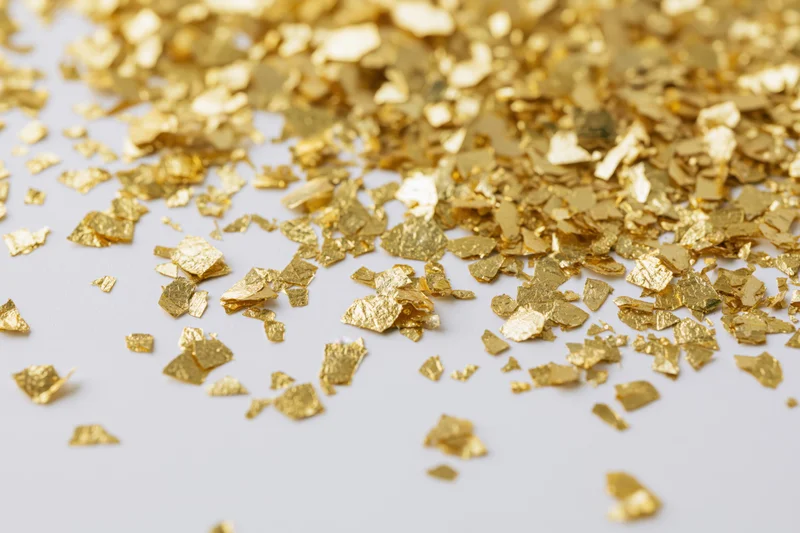 Scattered gold foil confetti pieces on a white surface