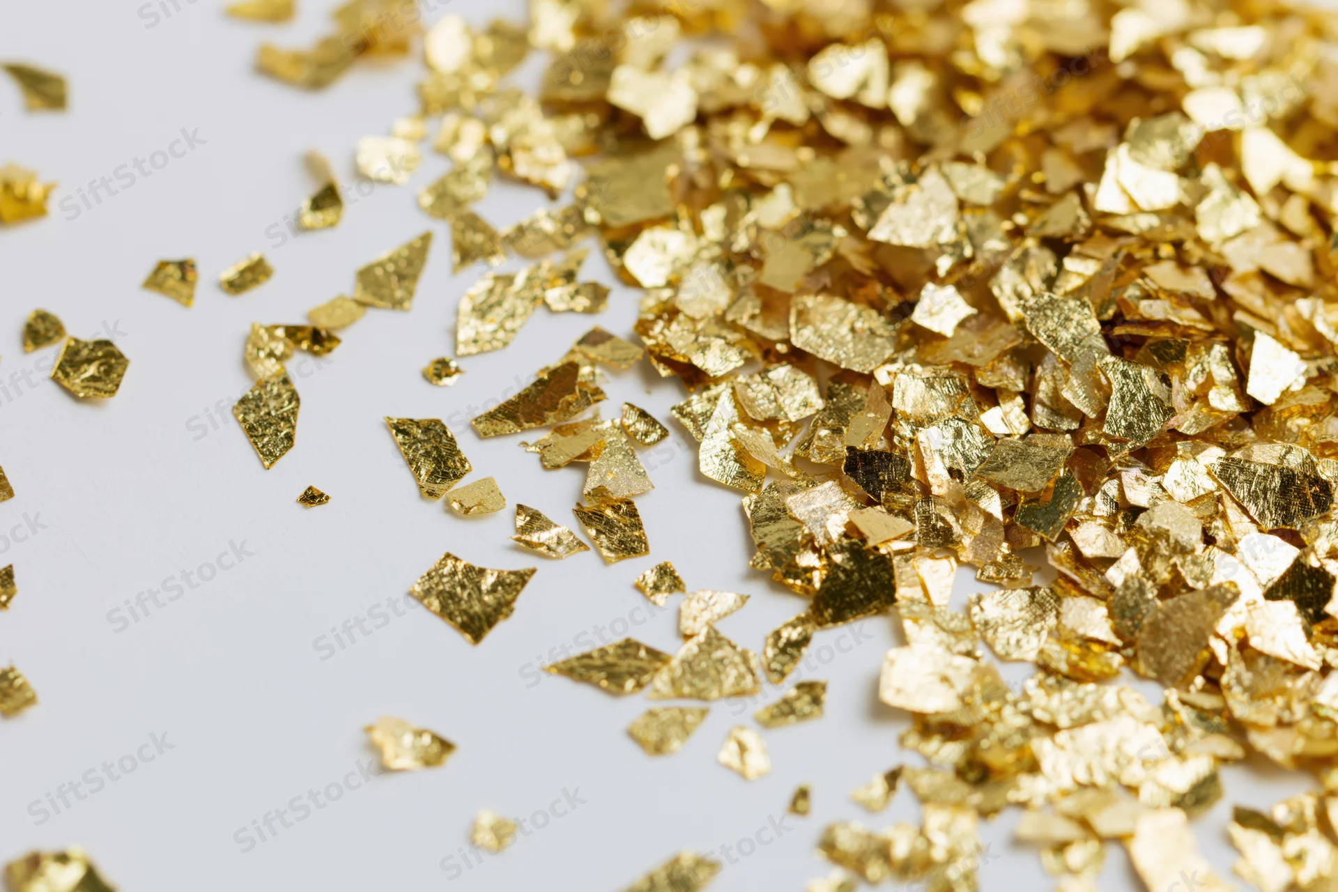 Gold foil confetti pieces scattered across a white surface with copyspace on the left