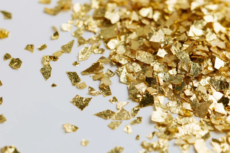 Gold foil confetti pieces scattered across a white surface with copyspace on the left