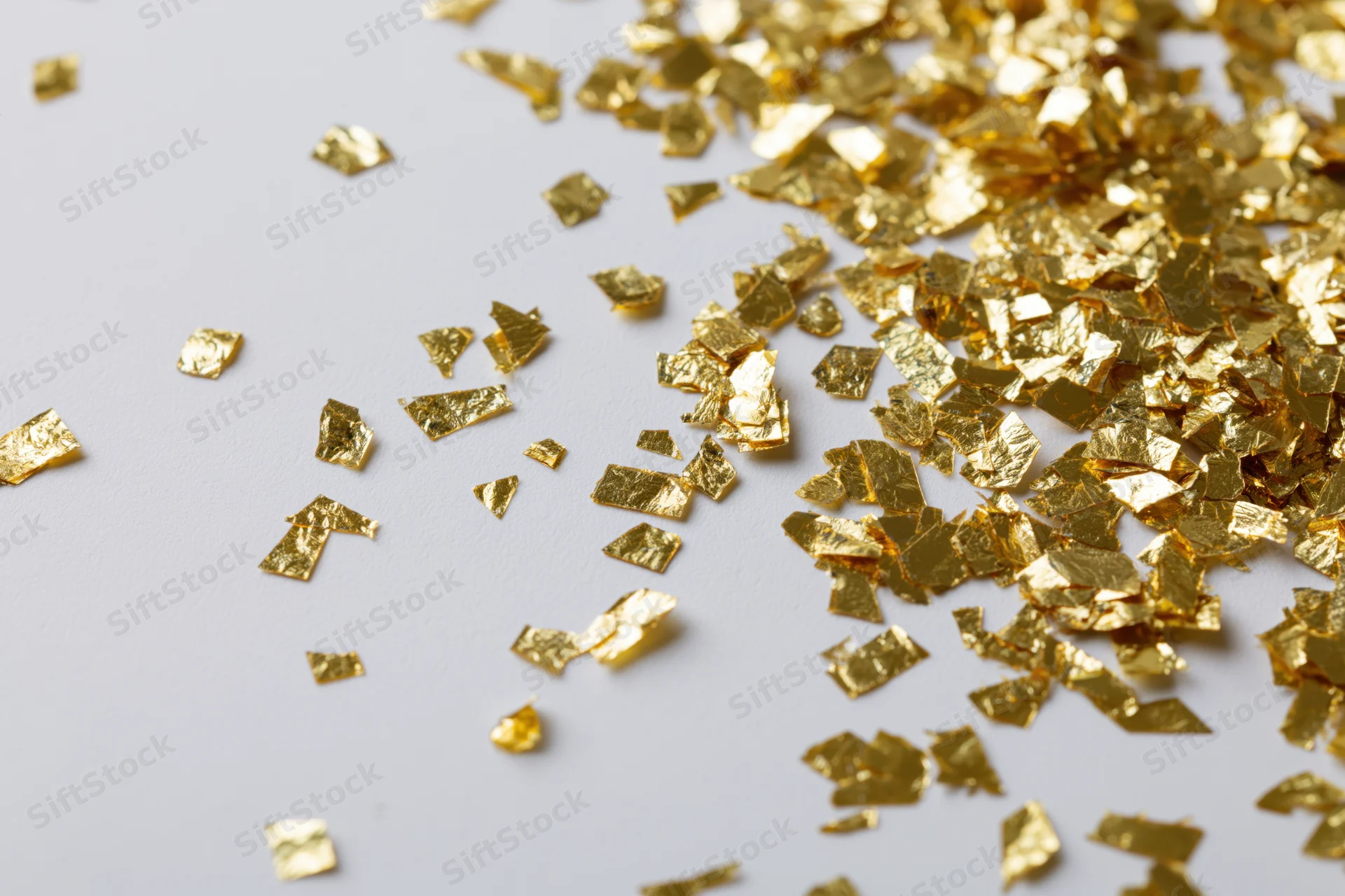 Scattered gold foil confetti on a white surface with copyspace