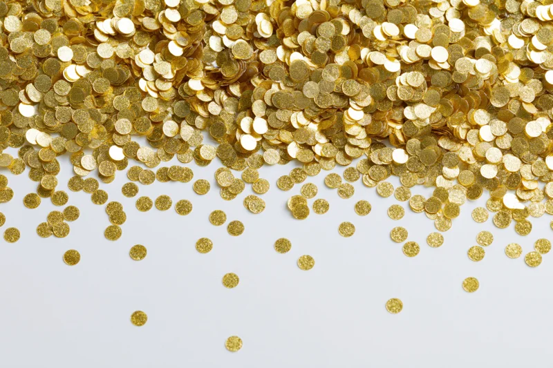 Gold confetti pieces scattered across a white surface with copyspace