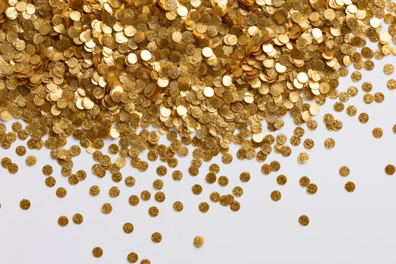 Gold confetti scattered across a white surface with copyspace