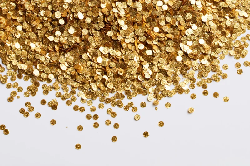 Gold confetti pieces scattered across a white surface with copyspace