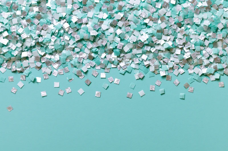 Square confetti pieces scattered densely at top and sparse at bottom on turquoise surface