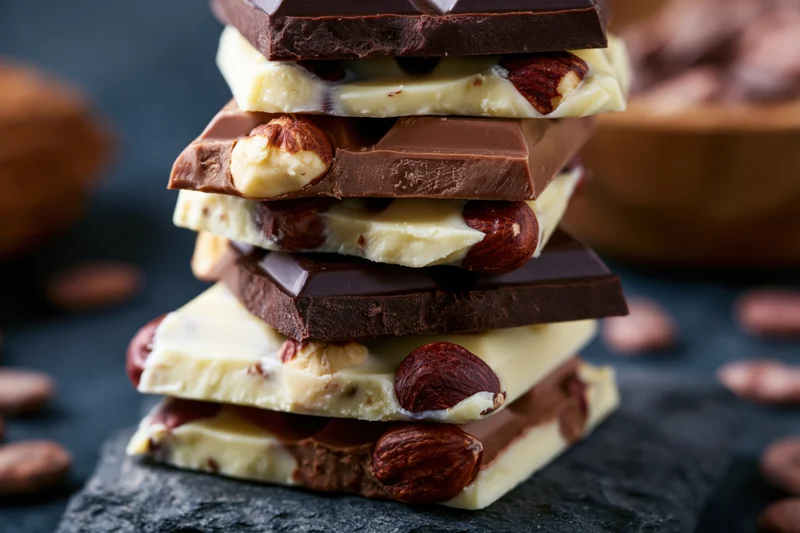 Stack of broken chocolate bar pieces layered with nuts on slate surface