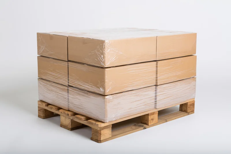 Stack of cardboard boxes wrapped in plastic on wooden pallet against white background