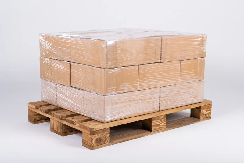 Stack of cardboard boxes wrapped in plastic on wooden pallet against white background