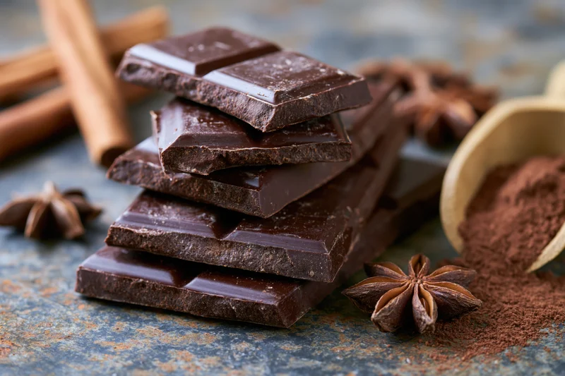 Broken dark chocolate pieces stacked on a rusty metal surface with cinnamon sticks and star anise nearby