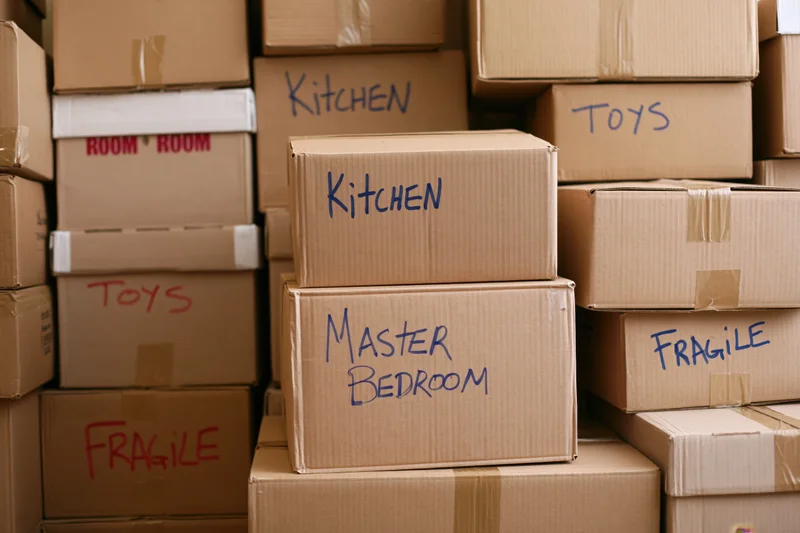 Stacked cardboard moving boxes labeled with room names and fragile warnings filling a storage space